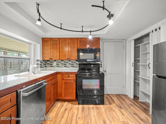 kitchen featuring black appliances, a textured ceiling, backsplash, a raised ceiling, and light wood-type flooring