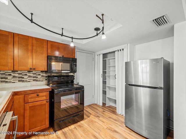 kitchen with light hardwood / wood-style floors, tile countertops, black appliances, a textured ceiling, and tasteful backsplash