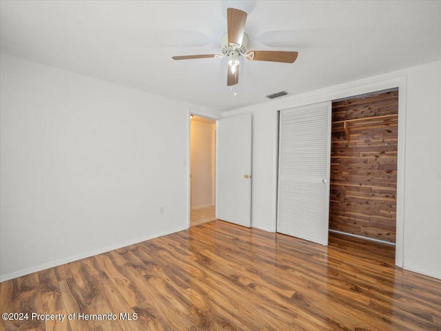 unfurnished bedroom featuring hardwood / wood-style floors, ceiling fan, wooden walls, and a closet