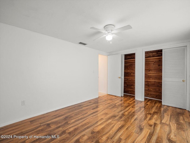 unfurnished bedroom with ceiling fan, multiple closets, and dark hardwood / wood-style flooring