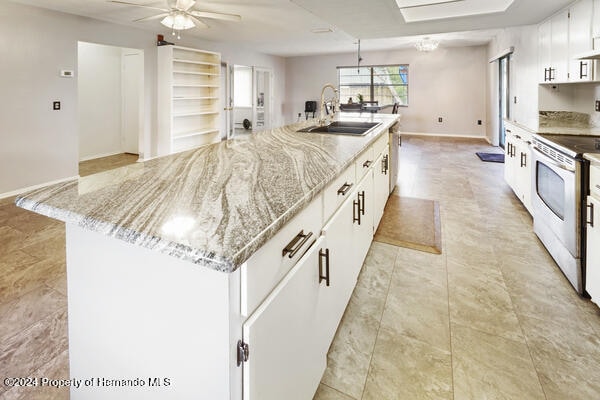 kitchen with white cabinetry, sink, light stone countertops, stainless steel electric range oven, and a kitchen island with sink