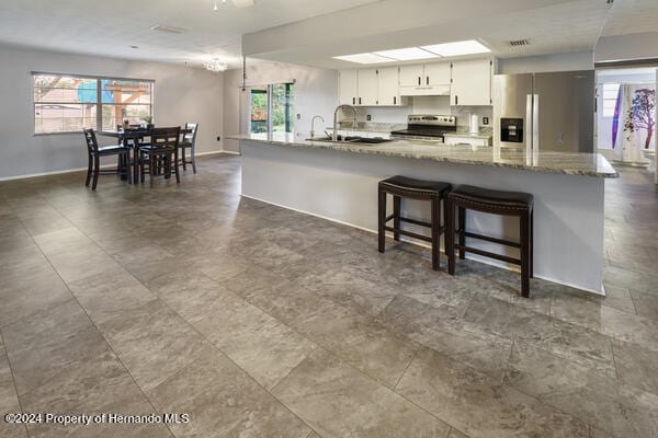 kitchen featuring white cabinetry, appliances with stainless steel finishes, stone counters, sink, and a breakfast bar area