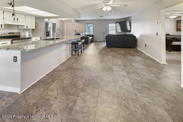 kitchen with stainless steel appliances, light stone countertops, sink, white cabinets, and a breakfast bar area