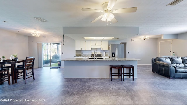 kitchen featuring white cabinetry, sink, light stone counters, a kitchen breakfast bar, and stainless steel fridge with ice dispenser