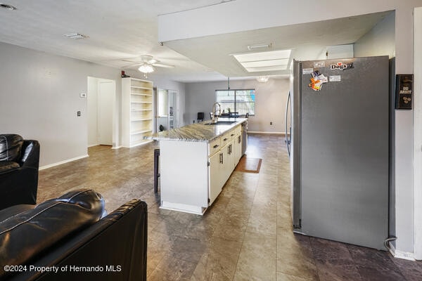 kitchen with white cabinetry, sink, ceiling fan, a center island, and stainless steel fridge