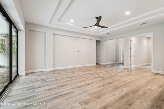 empty room with ceiling fan, a raised ceiling, and light wood-type flooring