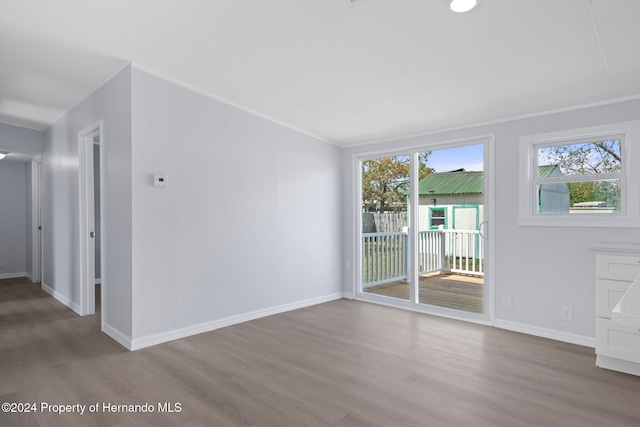 empty room featuring plenty of natural light, wood-type flooring, and crown molding