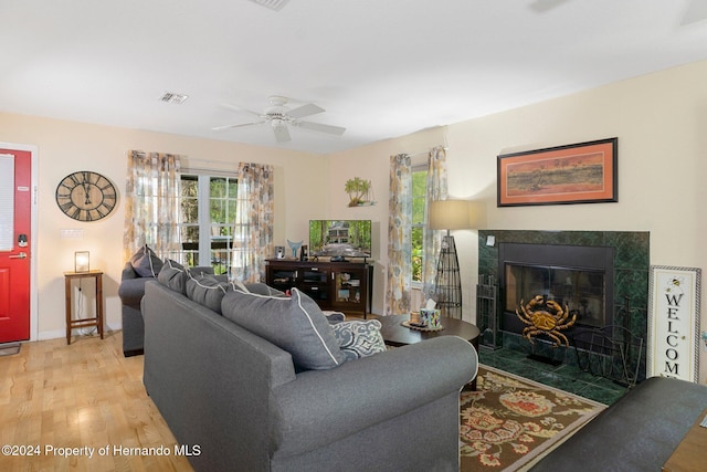 living room featuring a tiled fireplace, ceiling fan, and wood-type flooring