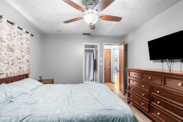 bedroom with a closet, a textured ceiling, light hardwood / wood-style floors, and ceiling fan