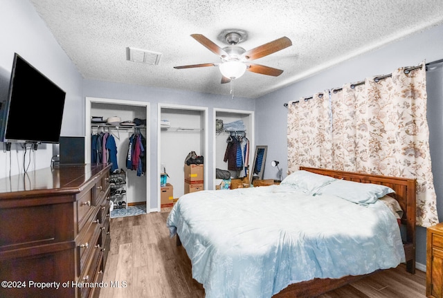 bedroom featuring hardwood / wood-style flooring, ceiling fan, a textured ceiling, and two closets