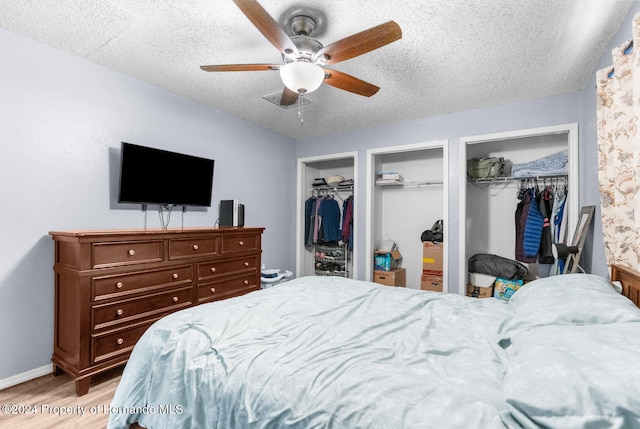 bedroom featuring ceiling fan, light hardwood / wood-style floors, a textured ceiling, and multiple closets