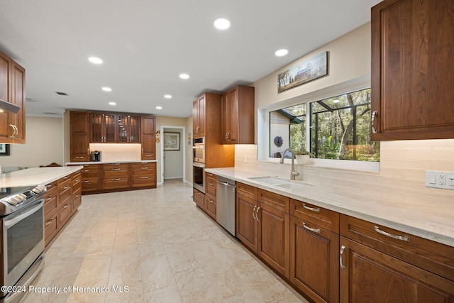 kitchen with backsplash, light stone countertops, sink, and appliances with stainless steel finishes