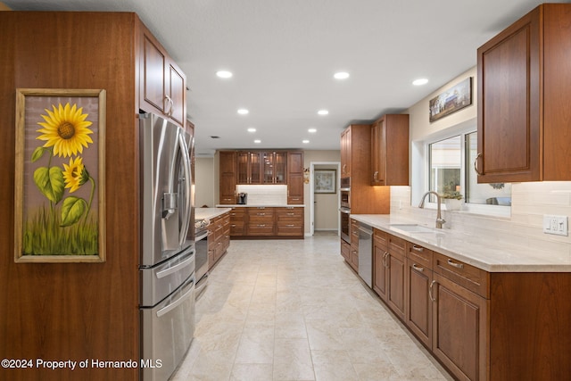 kitchen with backsplash, light stone countertops, sink, and appliances with stainless steel finishes