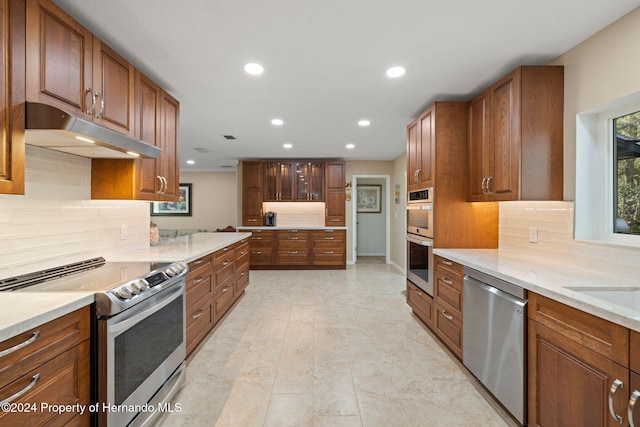 kitchen featuring decorative backsplash, light stone countertops, and stainless steel appliances