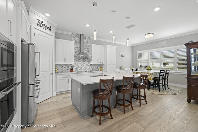 kitchen with white cabinets, a center island with sink, light hardwood / wood-style flooring, wall chimney exhaust hood, and decorative light fixtures