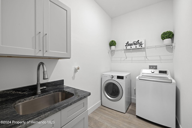 washroom featuring washer and dryer, cabinets, sink, and light hardwood / wood-style flooring