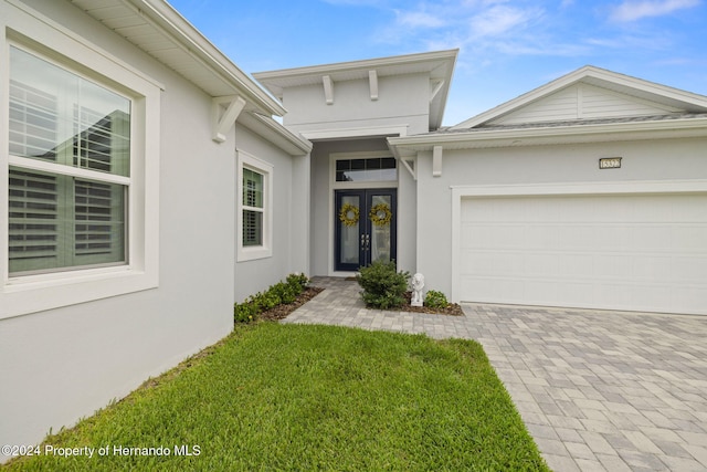 property entrance featuring a lawn, a garage, and french doors