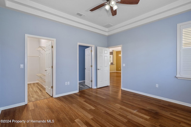 unfurnished bedroom featuring light hardwood / wood-style flooring, ceiling fan, a spacious closet, a tray ceiling, and a closet