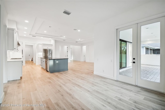 kitchen with french doors, white cabinets, a center island with sink, sink, and light wood-type flooring