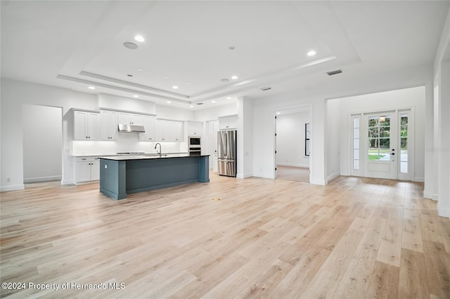 kitchen featuring white cabinets, a raised ceiling, a center island with sink, and stainless steel refrigerator