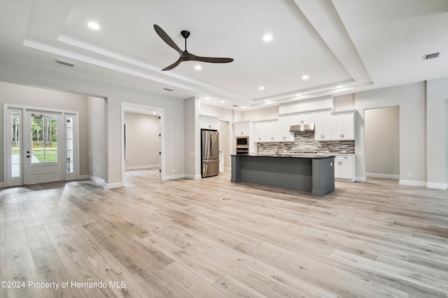 kitchen featuring a tray ceiling, white cabinets, an island with sink, and appliances with stainless steel finishes