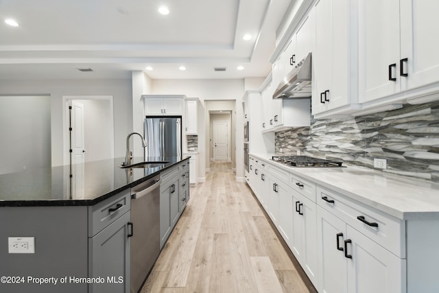 kitchen featuring white cabinets, range hood, appliances with stainless steel finishes, and dark stone counters