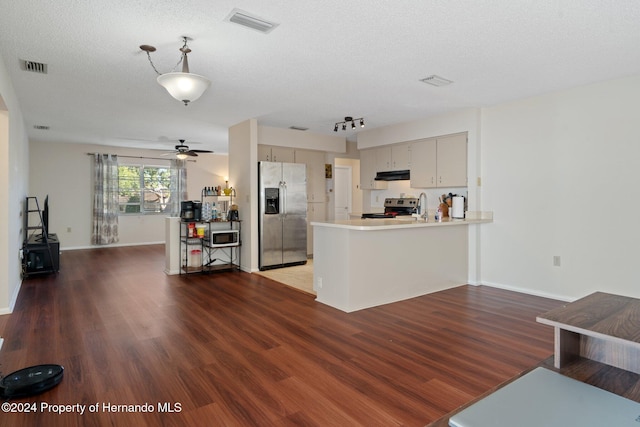 kitchen with a textured ceiling, kitchen peninsula, stainless steel appliances, and dark wood-type flooring