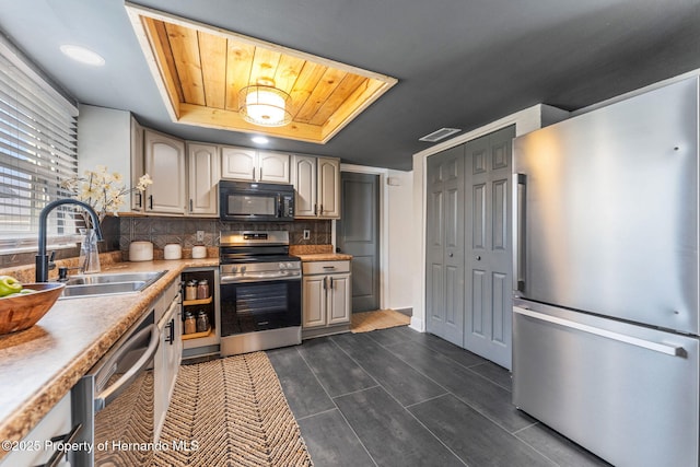 kitchen with tasteful backsplash, stainless steel appliances, a raised ceiling, and sink