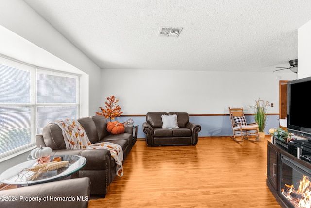 living room featuring ceiling fan, a textured ceiling, and light wood-type flooring