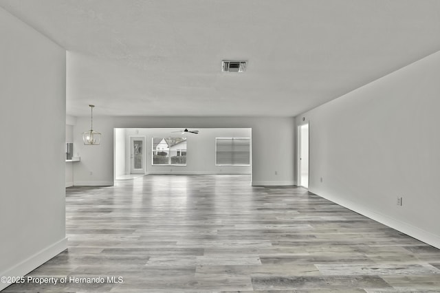 unfurnished living room featuring ceiling fan with notable chandelier and light wood-type flooring