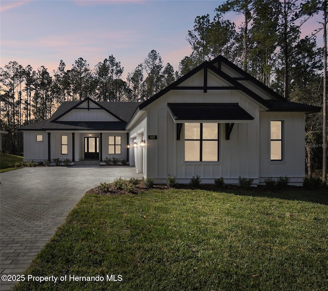 view of front of home featuring an attached garage, decorative driveway, a lawn, and board and batten siding