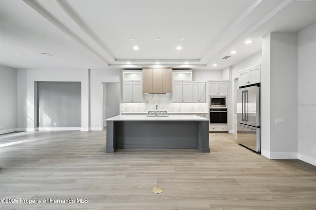 kitchen with a kitchen island with sink, high end refrigerator, built in microwave, black oven, and white cabinetry