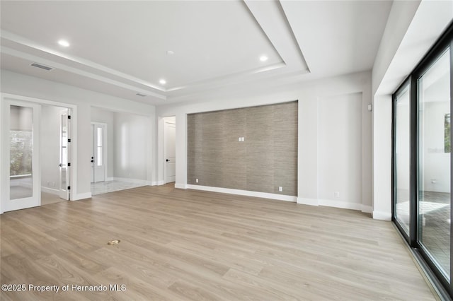 unfurnished living room featuring plenty of natural light, light hardwood / wood-style floors, french doors, and a tray ceiling