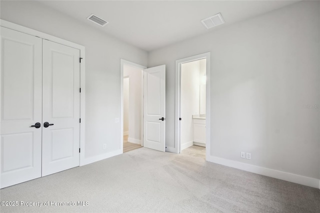 unfurnished bedroom featuring ensuite bathroom, a closet, and light colored carpet