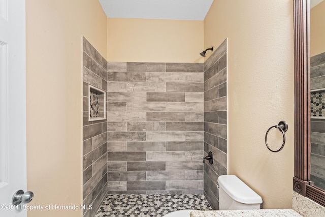 bathroom with a tile shower and toilet