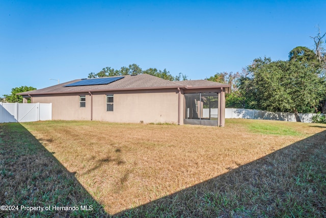 rear view of house with solar panels, a yard, and a sunroom