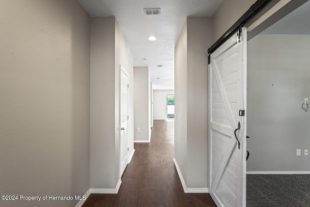 hall featuring a textured ceiling, a barn door, and dark wood-type flooring