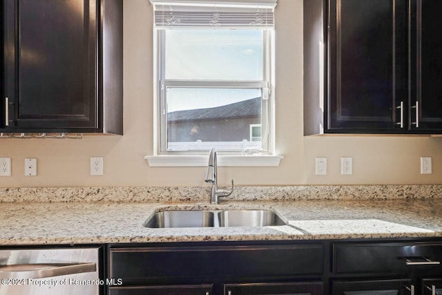 kitchen with stainless steel dishwasher, light stone countertops, and sink