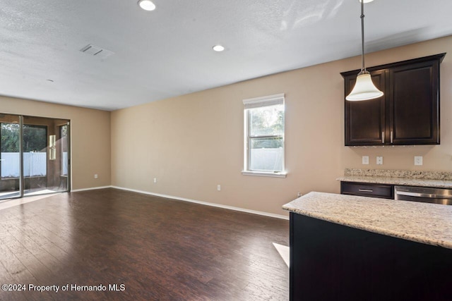 kitchen featuring dark wood-type flooring, stainless steel dishwasher, decorative light fixtures, light stone counters, and dark brown cabinets