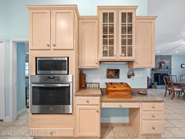 kitchen with a fireplace, light tile patterned flooring, stainless steel appliances, and light brown cabinetry