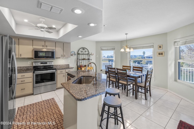 kitchen with sink, stainless steel appliances, dark stone counters, decorative light fixtures, and ceiling fan with notable chandelier