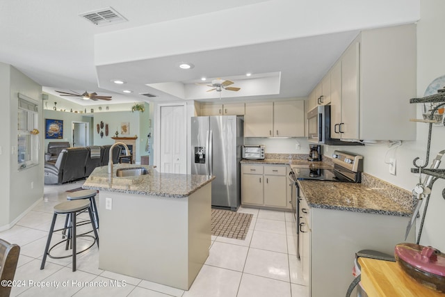 kitchen featuring sink, a raised ceiling, dark stone counters, a breakfast bar area, and appliances with stainless steel finishes