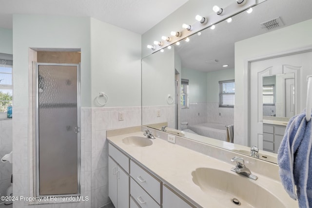 bathroom featuring shower with separate bathtub, vanity, a textured ceiling, and tile walls