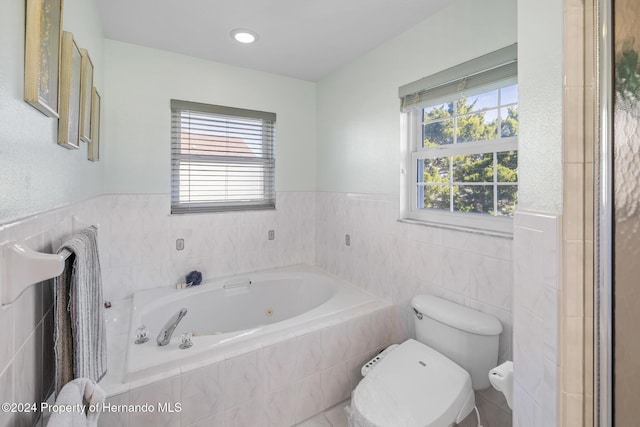 bathroom with a relaxing tiled tub, toilet, and tile walls