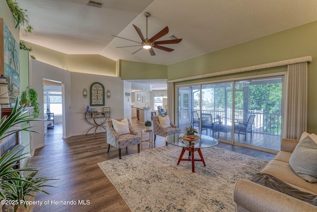 living room with a ceiling fan, vaulted ceiling, visible vents, wood finished floors, and baseboards