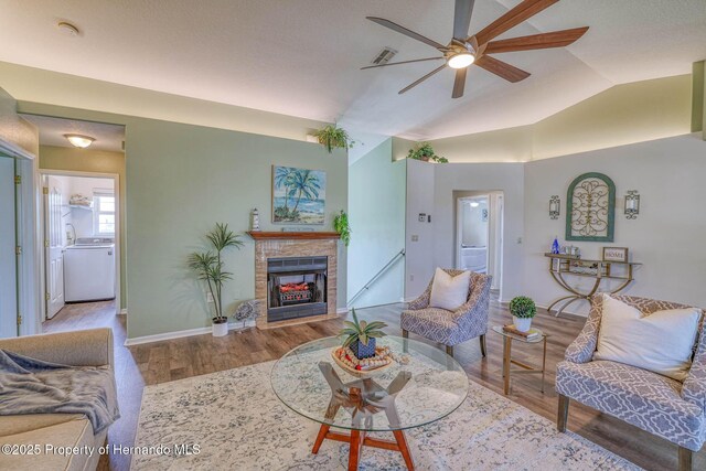 living room featuring a fireplace, a ceiling fan, vaulted ceiling, visible vents, and wood finished floors