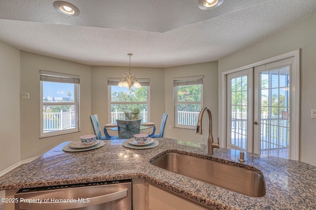 kitchen featuring dark stone counters, a textured ceiling, dishwasher, a sink, and hanging light fixtures