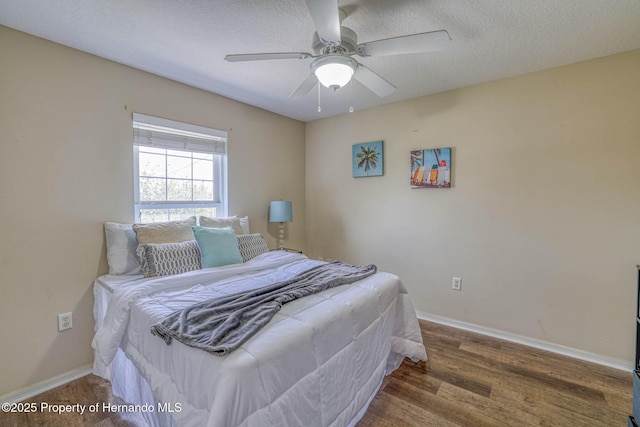 bedroom with a textured ceiling, wood finished floors, baseboards, and a ceiling fan