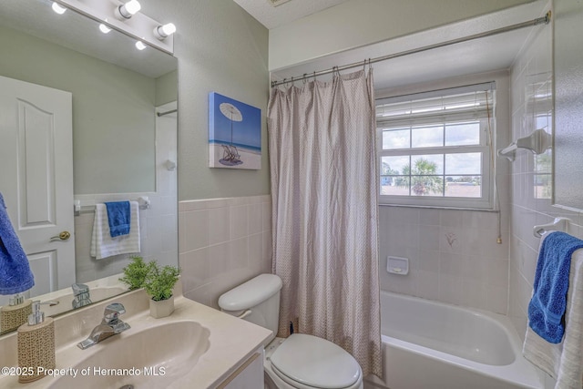 full bathroom featuring shower / bathtub combination with curtain, vanity, toilet, wainscoting, and tile walls