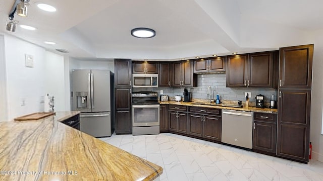 kitchen with appliances with stainless steel finishes, backsplash, light stone counters, and dark brown cabinets